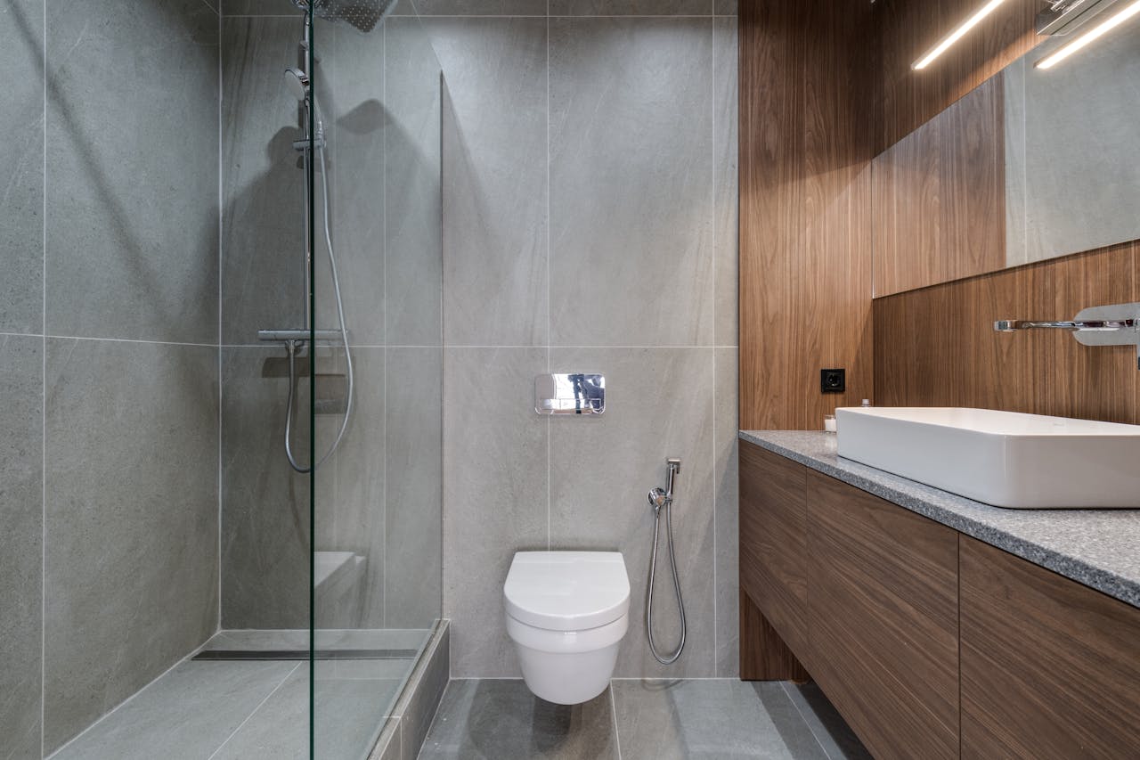 home-hero Elegant modern bathroom featuring a walk-in shower, sink, and toilet with a stylish wooden finish.